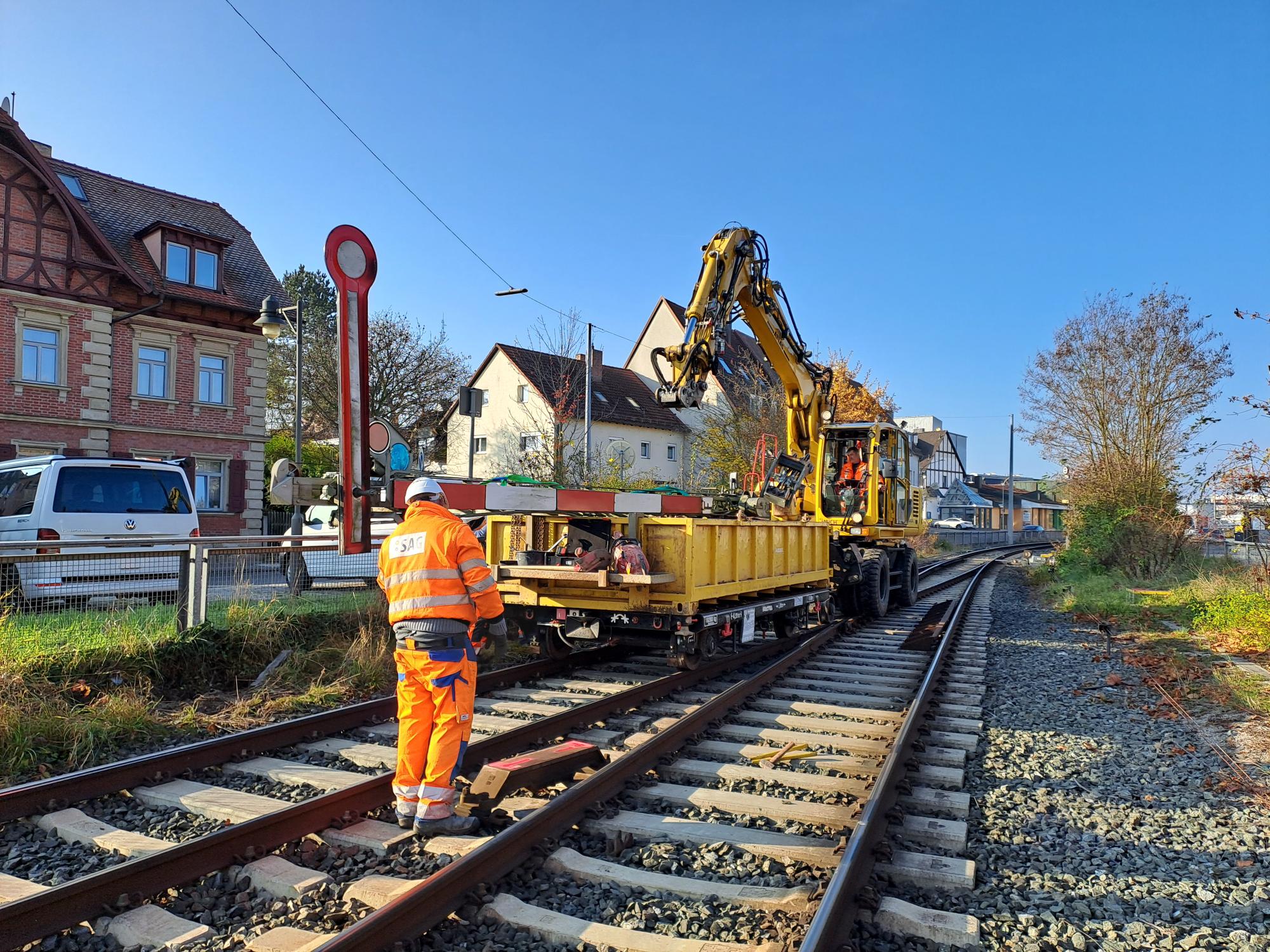 Baustellenfahrzeug mittig auf Gleis, Bauarbeiter:in in orangenem Anzug vorne