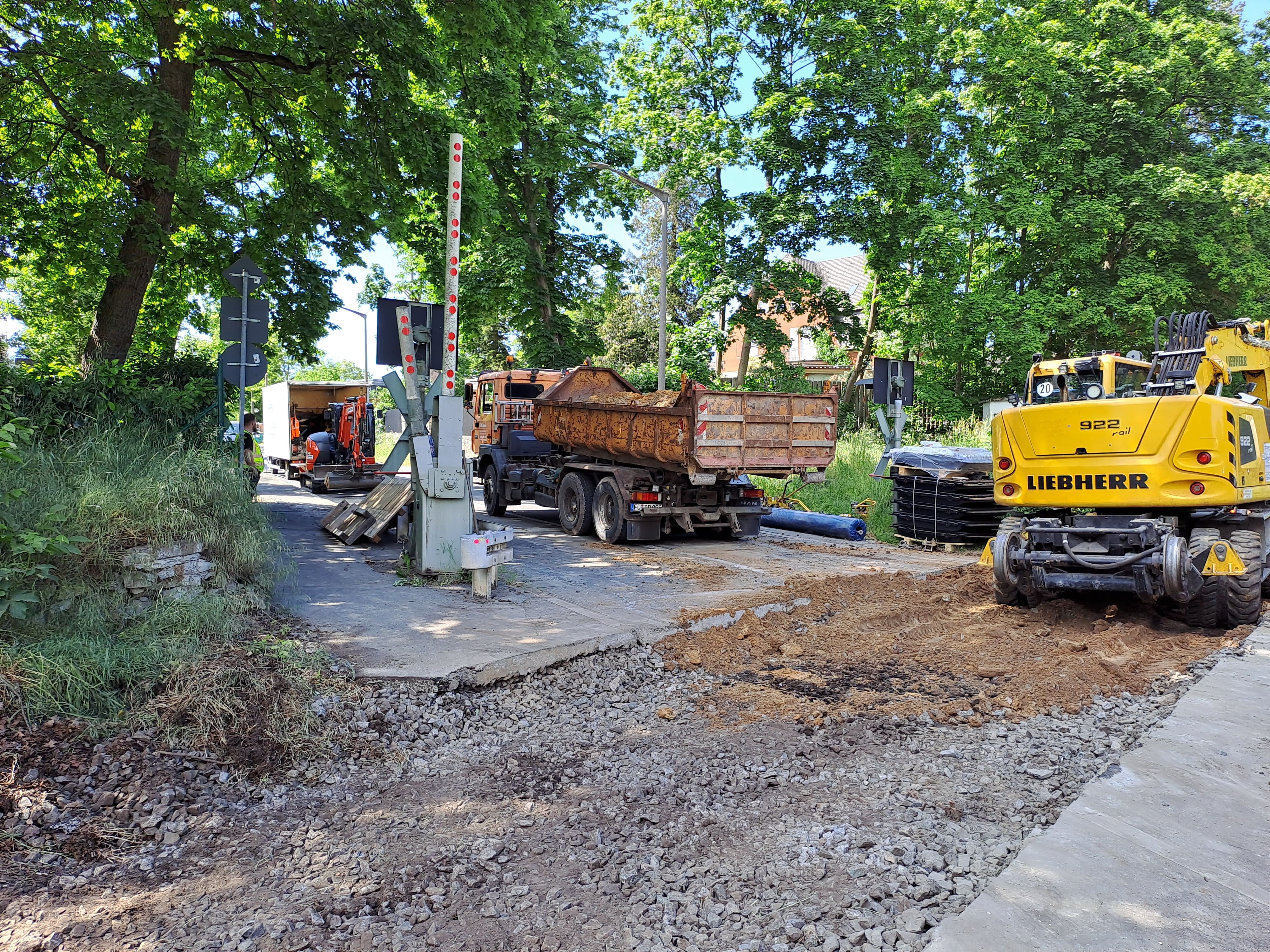 Zu sehen ist eine Baustelle mit einem Bagger und Laster an einem Bahnübergang