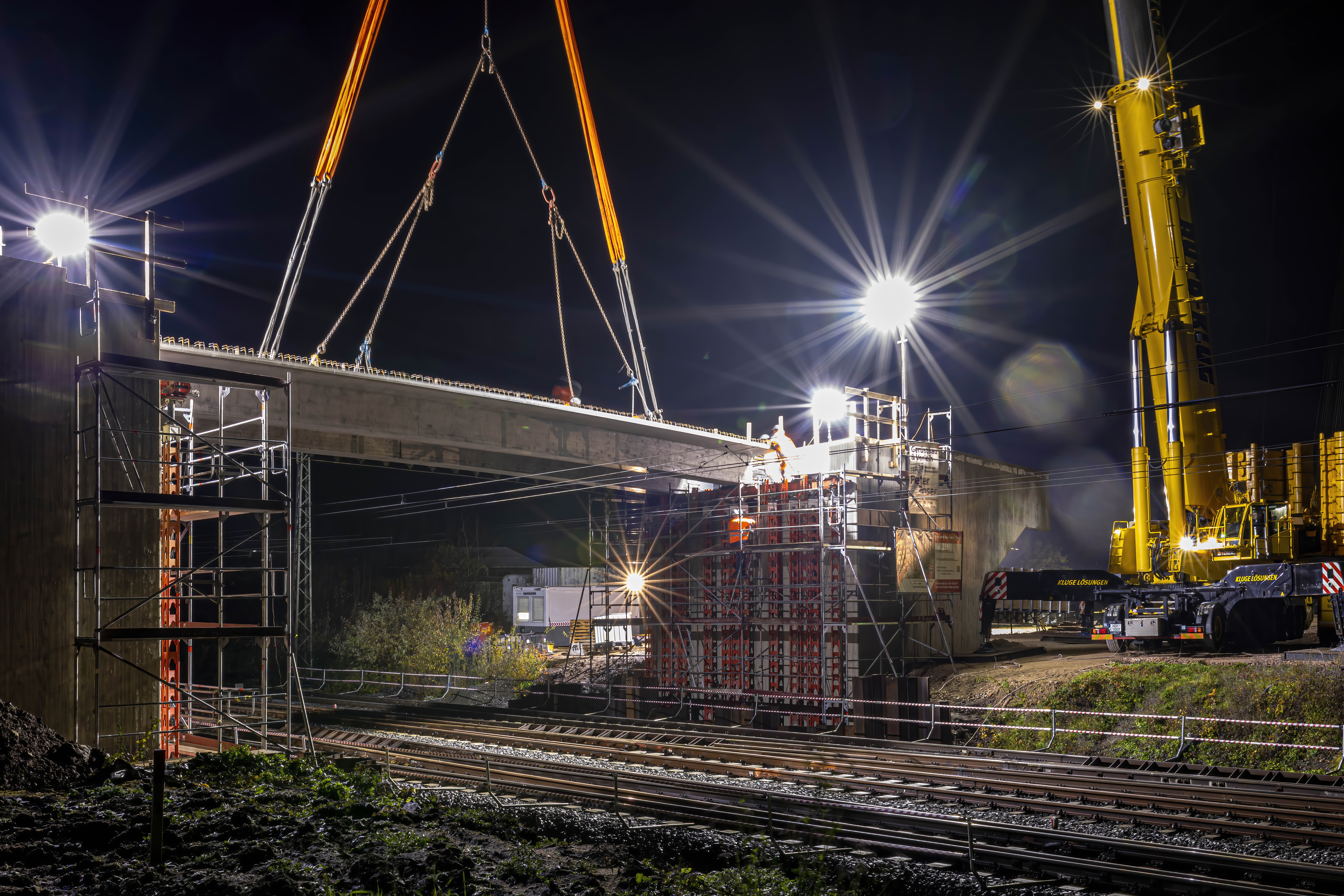 Bei Nacht wird eine Brücke über eine zweigleisigen Bahnstrecke mit großen Maschinen eingehoben.